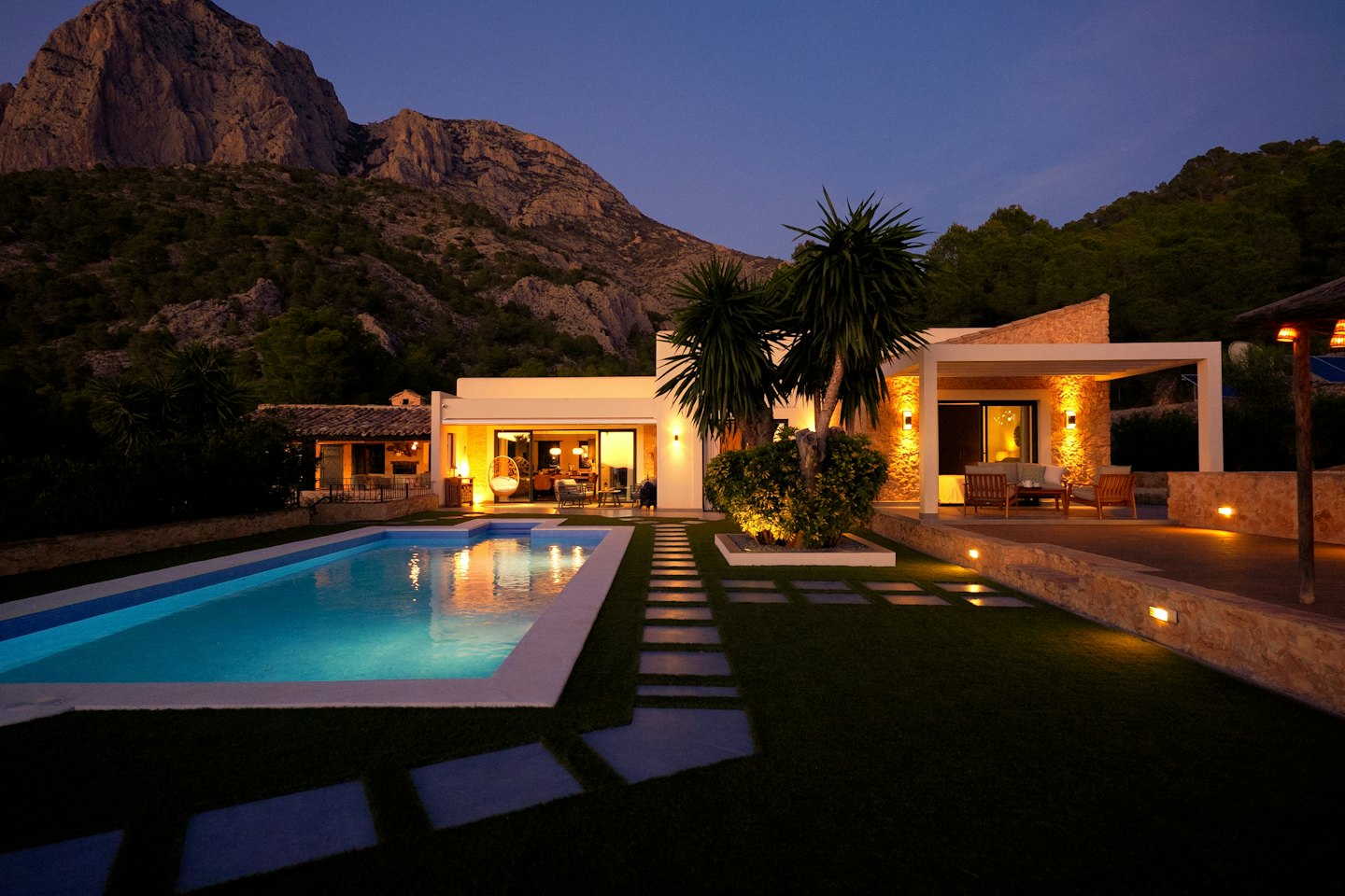 Villa moderna con piscina al tramonto con montagne sullo sfondo.