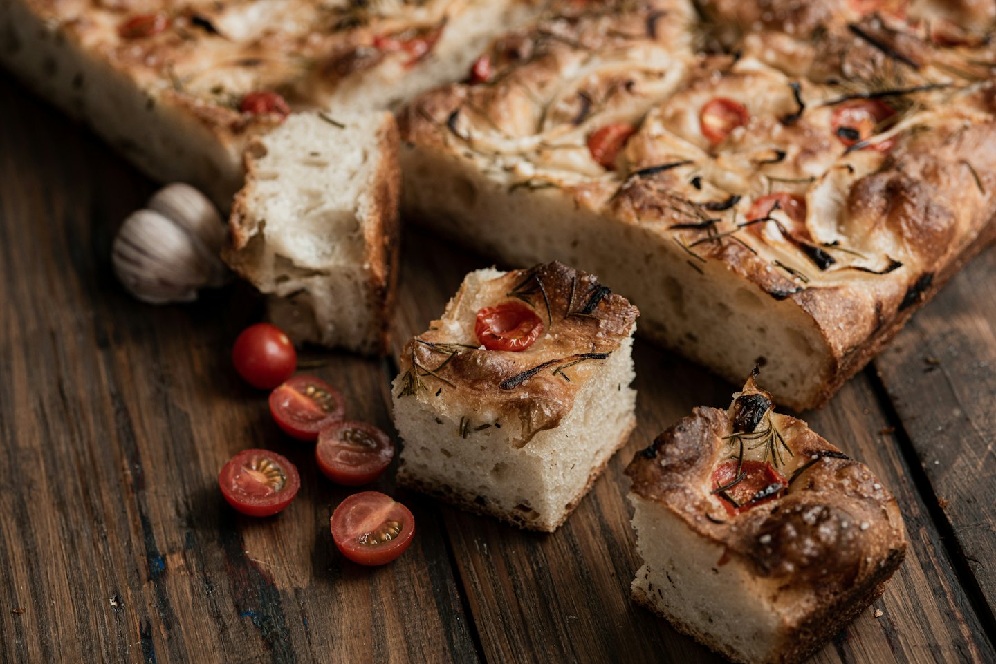 Focaccia appena sfornata con pomodori e rosmarino su un tagliere di legno.