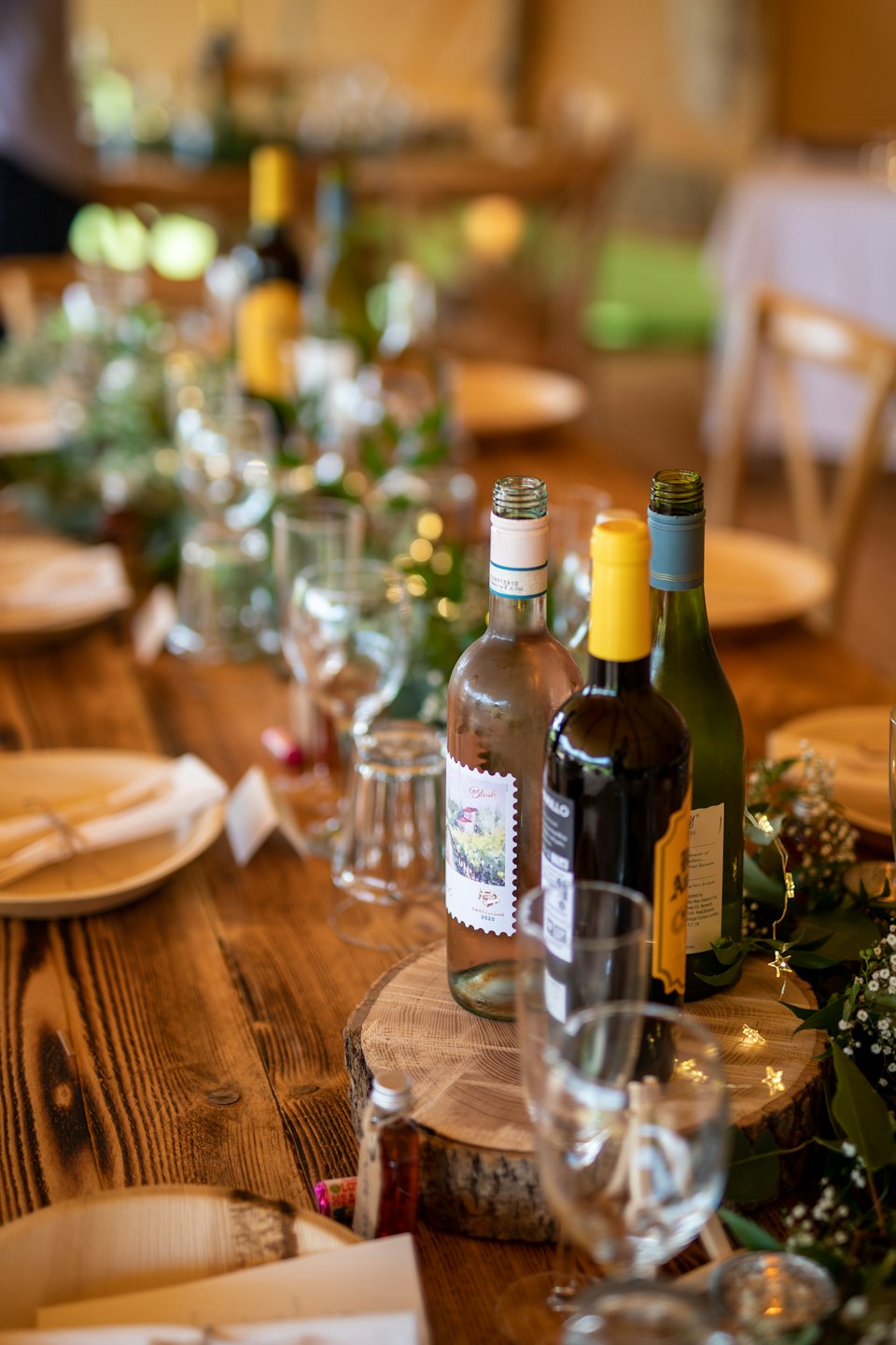 Tavola rustica apparecchiata per un evento con vino, piatti e fogliame.